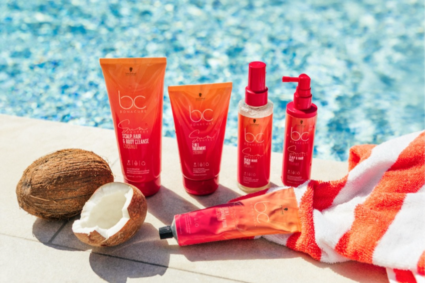 Productos de la gama Bonacure Sun Protect de Schwarzkopf Professional sobre una superficie junto a una piscina, con coco y toalla de playa, enfocados en el cuidado capilar en verano.