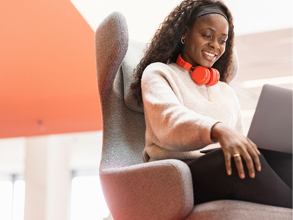 Una empleada de Henkel está sentada en una cómoda silla con su ordenador portátil sobre las rodillas y sonríe.