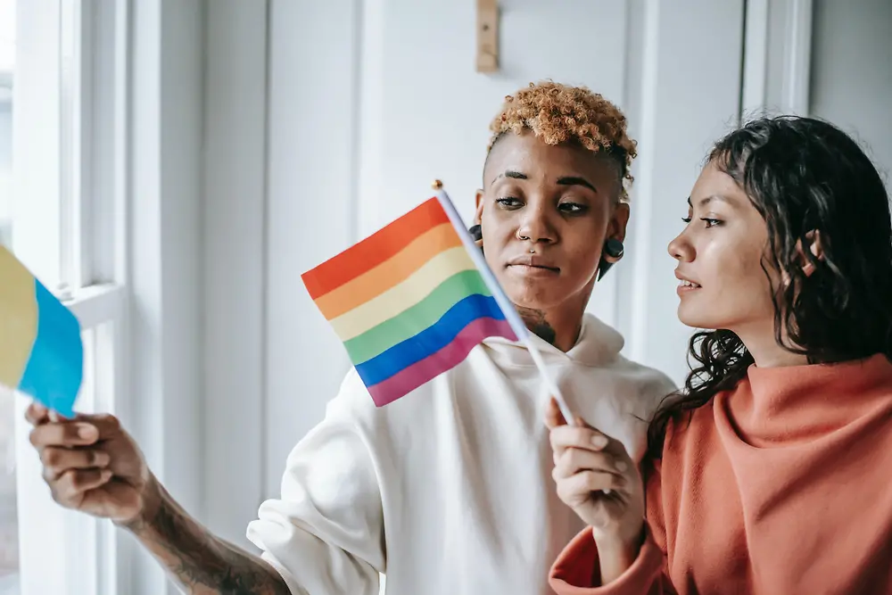 Dos mujeres hablan mientras sostienen una bandera LGBTQ+.