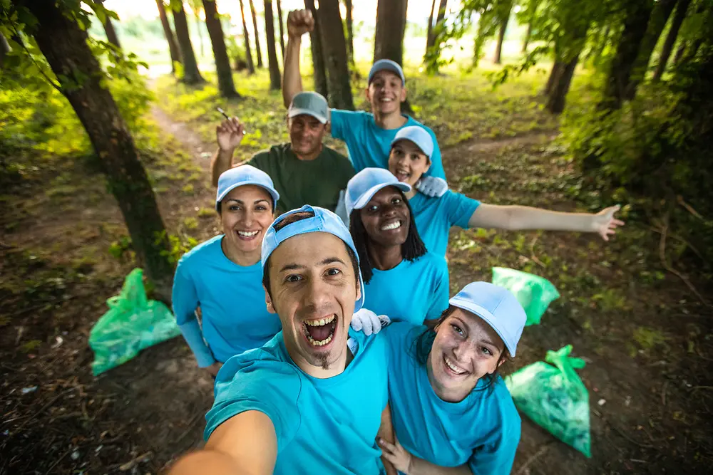 Un grupo de voluntarios se toma una selfie en el bosque con bolsas de basura llenas a su lado.