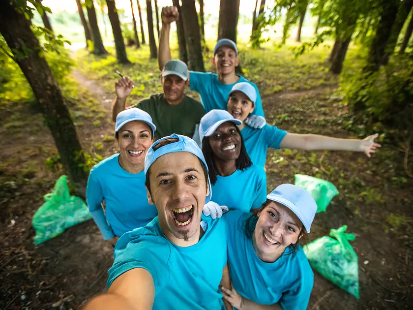 Un grupo de voluntarios se toma una selfie en el bosque con bolsas de basura llenas a su lado.