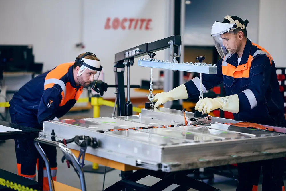 Técnicos trabajando en la reparación de una batería de vehículo eléctrico en un taller, utilizando herramientas y equipos especializados.