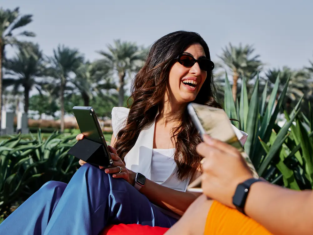 Mujer trabajando con un portátil al aire libre en un parque soleado, lo que refleja las opciones de trabajo flexibles y la cultura laboral moderna de Henkel.