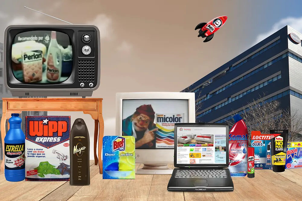 Imagen con productos icónicos de Henkel Ibérica sobre una mesa, incluyendo detergentes Wipp Express, Perlan, Micolor, limpiador Biff y adhesivos Loctite y Pritt. Al fondo se observa una televisión retro con un anuncio antiguo de Perlan, un portátil abierto y parte del edificio corporativo de Henkel. También aparece un cohete ilustrado con el logo de Pritt sobre un cielo azul. Ideal para destacar la historia y evolución de Henkel, líder en productos de limpieza, adhesivos y cuidado del hogar.