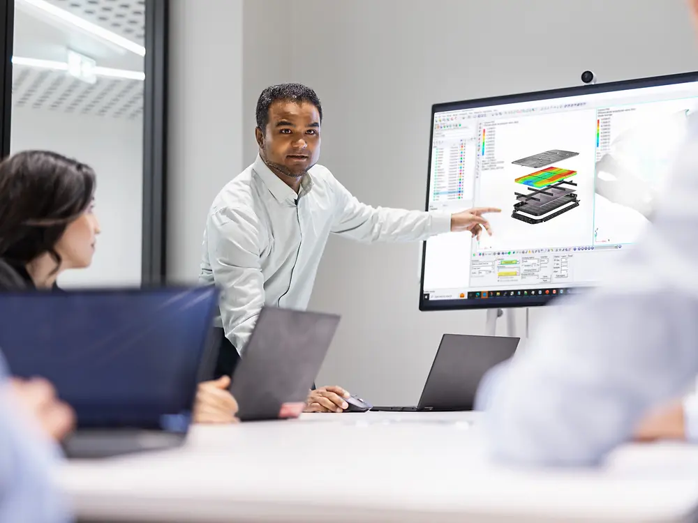 Equipo colaborando en innovación utilizando soluciones Loctite, con un profesional presentando diseños de modelado y simulación en una pantalla grande durante una reunión técnica.