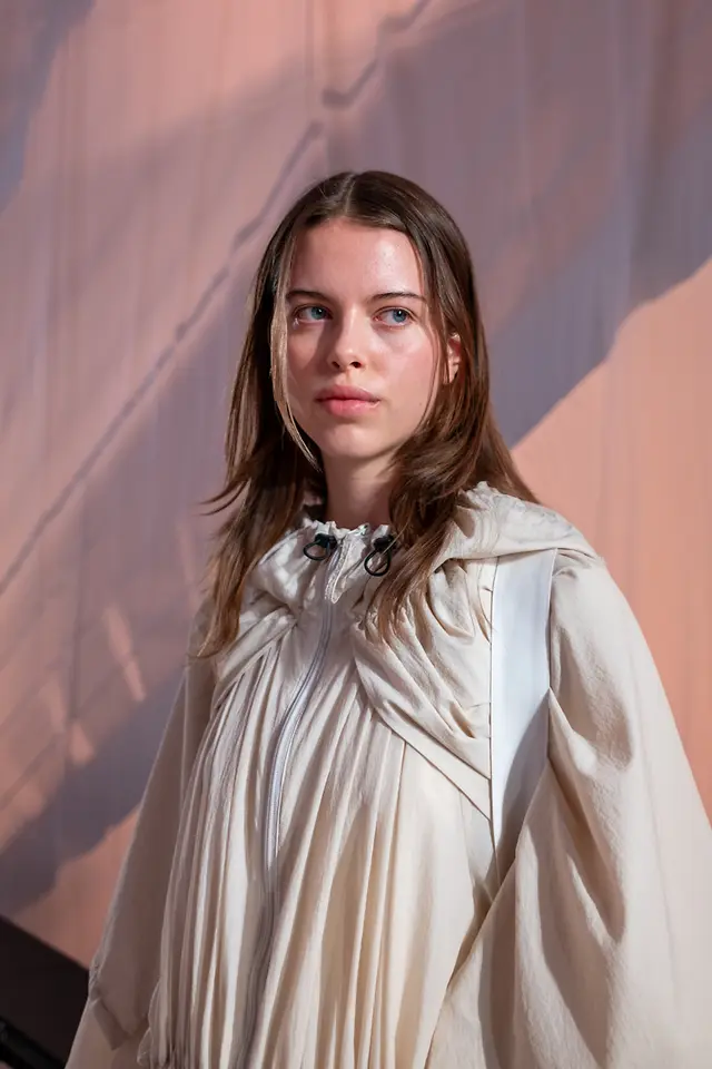 Modelo con el cabello peinado de forma natural y vestuario en tonos claros durante el desfile OI26.