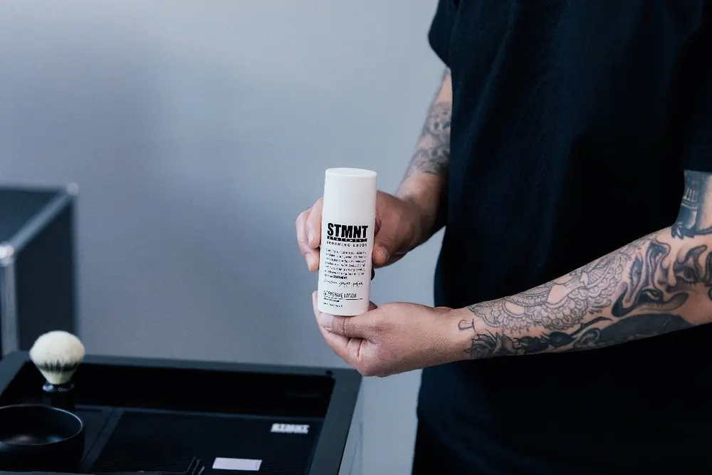 Barbero sosteniendo una loción aftershave de STMNT Grooming Goods, producto de cuidado masculino recomendado como regalo para el Día del Padre.