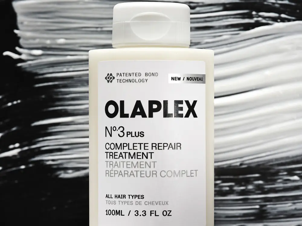 Envase del tratamiento Olaplex Nº3 Plus sobre un fondo texturizado en blanco y negro.