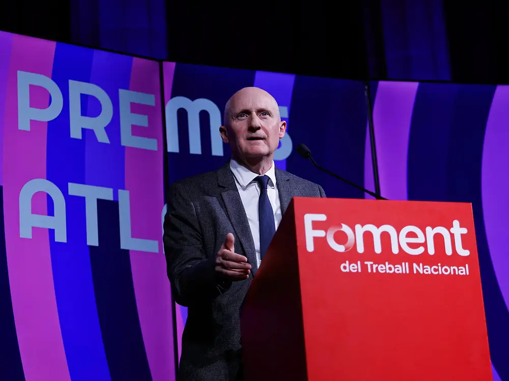 Pódium con un orador hablando desde un atril rojo con el logotipo de “Foment del Treball Nacional”, durante la ceremonia de entrega de los XII Premios Atlante, con un fondo iluminado en tonos azul y morado donde se lee “Premis Atlante”.