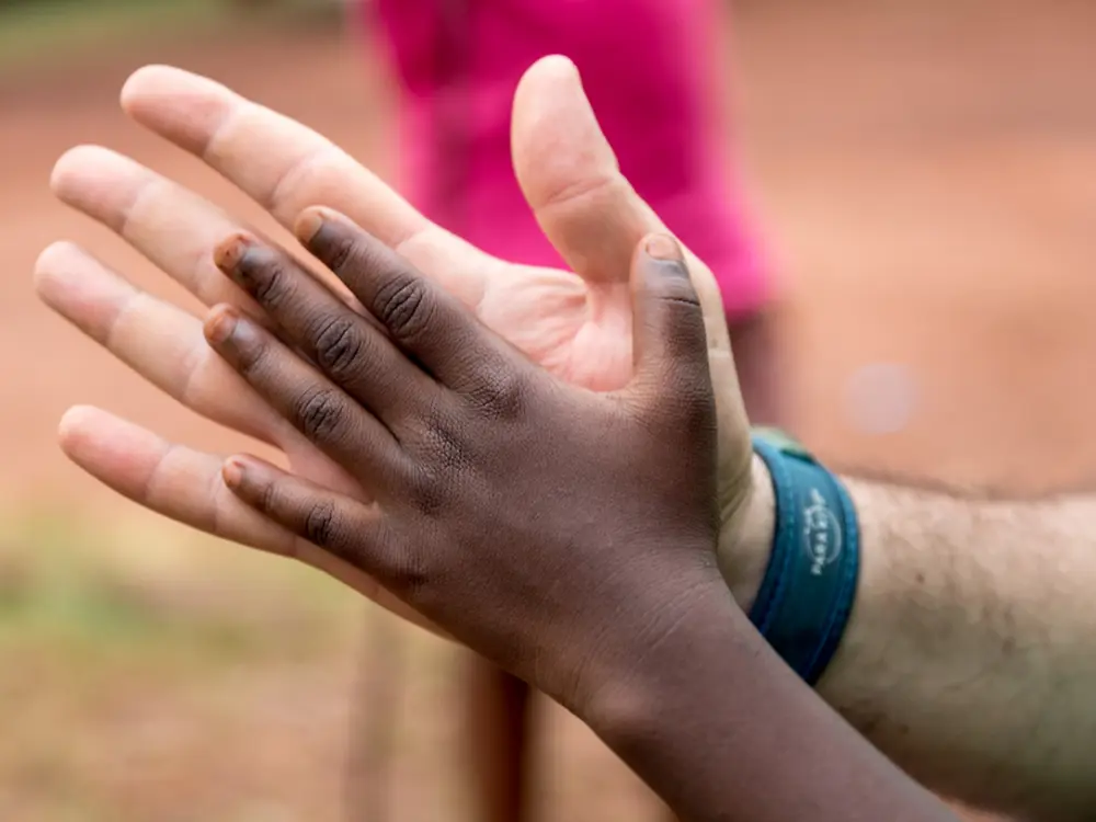 Imagen de una mano levantada, con una pulsera azul en la muñeca, en un entorno exterior, representando simbólicamente la participación en acciones de voluntariado del programa MIT de Henkel.