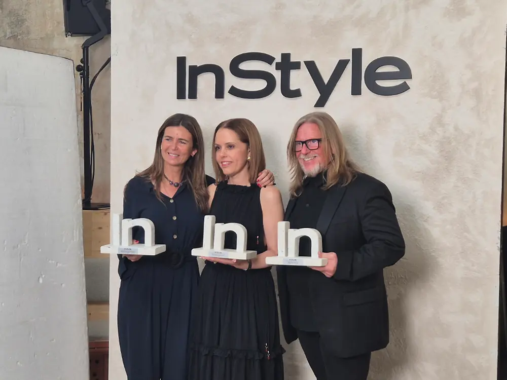 Imagen de tres personas posando frente a un panel con el logotipo de InStyle, sosteniendo trofeos de los premios Belleza con Influencia, en un ambiente de ceremonia y entrega de galardones.
