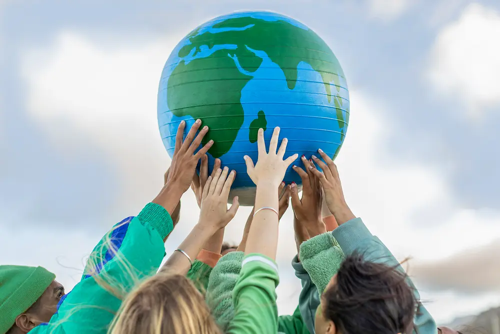 Varias personas levantan un globo terráqueo azul y verde hacia el cielo, simbolizando los objetivos globales de sostenibilidad y cero emisiones netas de Henkel para 2045. 