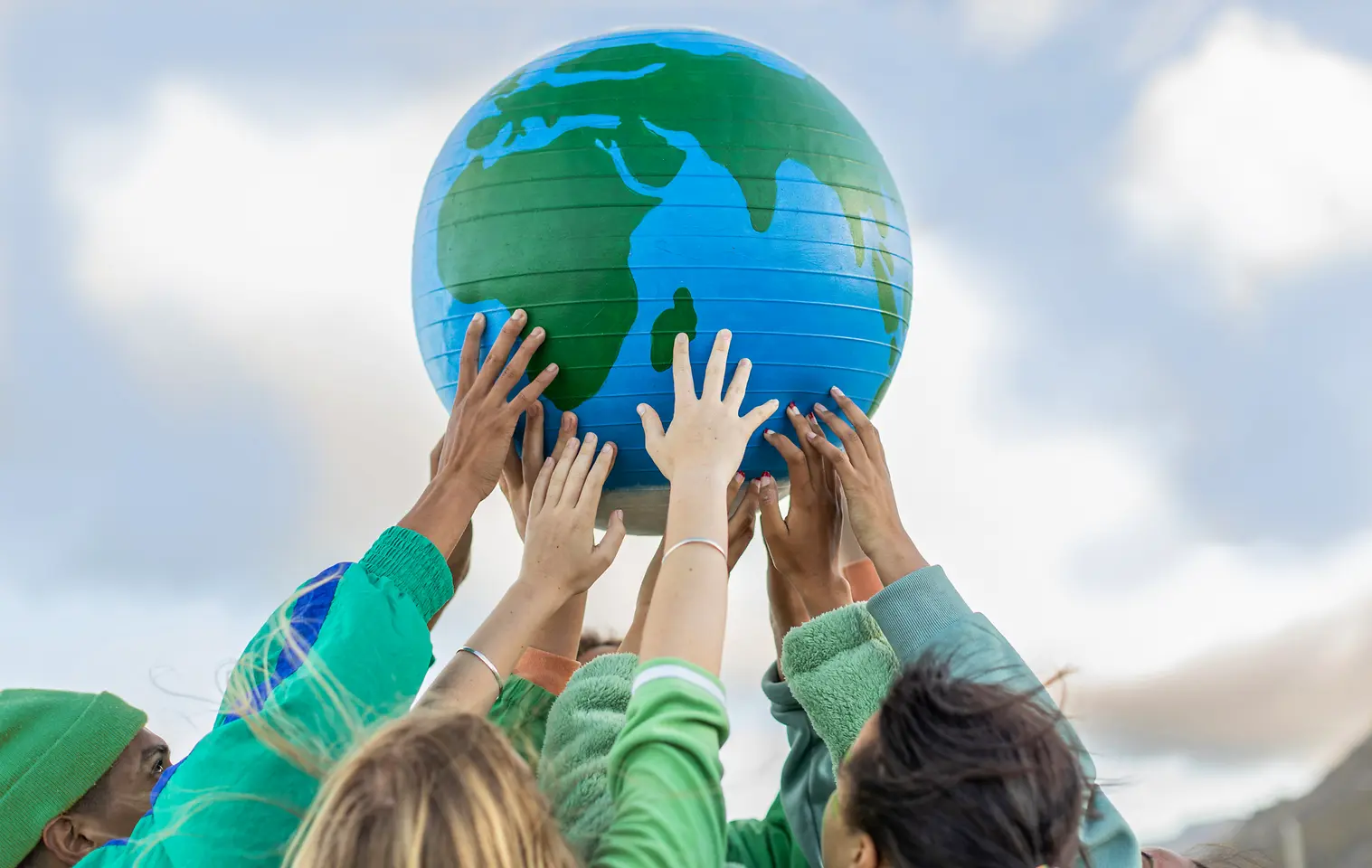 Varias personas levantan un globo terráqueo azul y verde hacia el cielo, simbolizando los objetivos globales de sostenibilidad y cero emisiones netas de Henkel para 2045. 