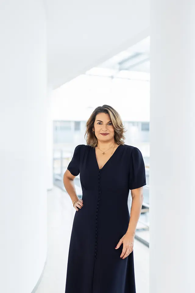 Retrato corporativo de Sylvie Nicol, directiva de Henkel, con blusa azul oscuro y cabello castaño, posando en una oficina luminosa.