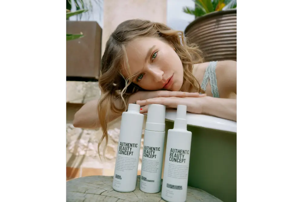 Modelo apoyada junto a productos de la gama Amplify de Authentic Beauty Concept en un entorno natural, mostrando una rutina de cuidado capilar para cabello fino.