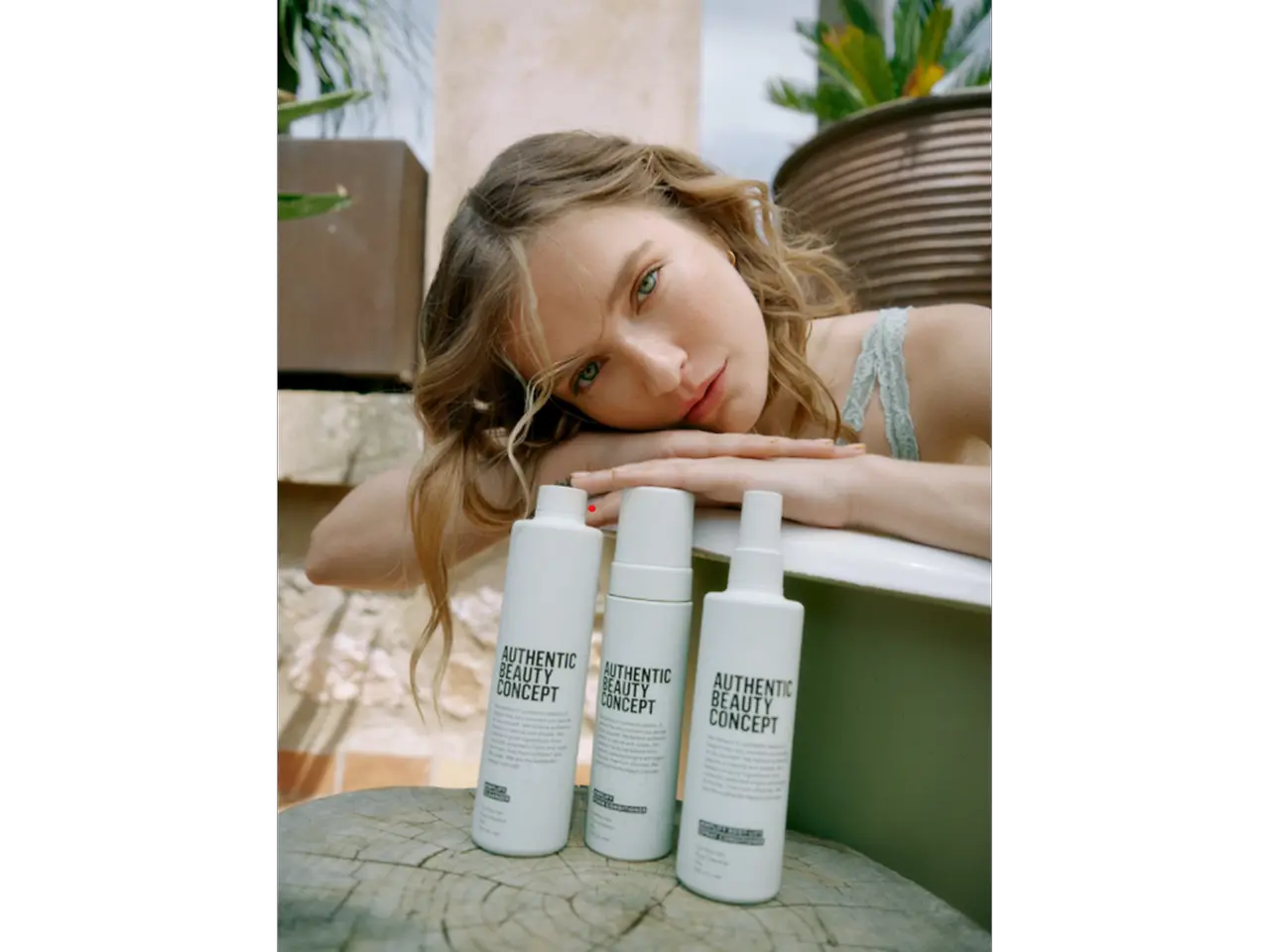Modelo apoyada junto a productos de la gama Amplify de Authentic Beauty Concept en un entorno natural, mostrando una rutina de cuidado capilar para cabello fino.