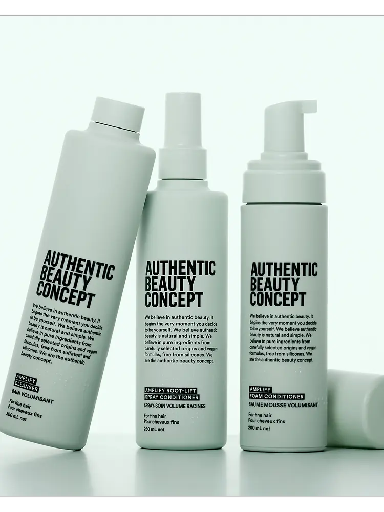 Tres productos de la gama Amplify de Authentic Beauty Concept sobre fondo neutro, incluyendo champú, spray acondicionador y acondicionador en espuma para cabello fino.
