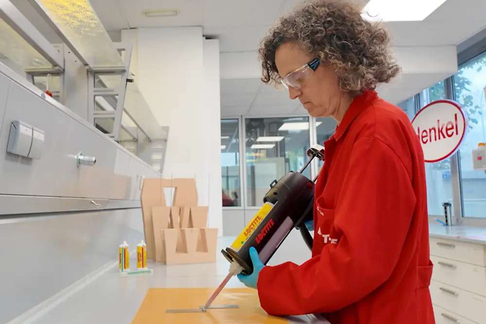 Entorno de laboratorio donde se aplica adhesivo con herramienta de precisión sobre piezas en una mesa de trabajo durante pruebas técnicas.