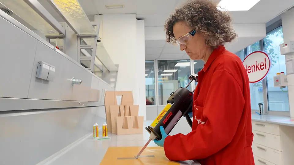Entorno de laboratorio donde se aplica adhesivo con herramienta de precisión sobre piezas en una mesa de trabajo durante pruebas técnicas.