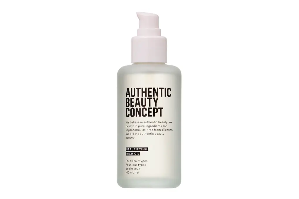 Botella del Aceite Embellecedor Intensivo de Authentic Beauty Concept con dispensador, envase translúcido con etiqueta negra sobre fondo blanco neutro.
