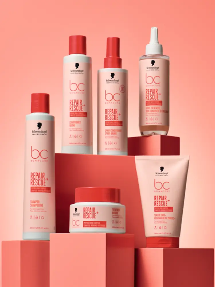 Productos de la gama Bonacure Repair Rescue+ de Schwarzkopf Professional sobre un fondo rosa, incluyendo champú, acondicionador, spray acondicionador y el nuevo Tratamiento Iluminador, diseñados para reparar y fortalecer el cabello dañado