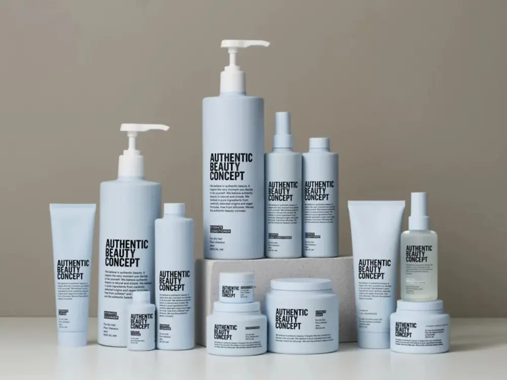 Productos de la gama Hydrate de Authentic Beauty Concept dispuestos sobre una superficie neutra, incluyendo champú, acondicionador, mascarilla, spray acondicionador, loción y tratamientos hidratantes para el cuidado del cabello.