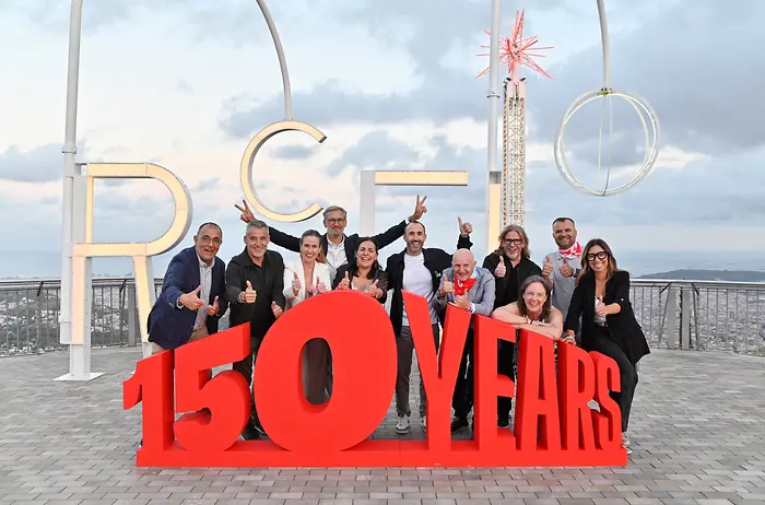 Integrantes del equipo directivo de Henkel Ibérica posan junto a una estructura con el mensaje “150 YEARS” durante el festival conmemorativo del 150 aniversario de Henkel, celebrado en Barcelona, con vistas panorámicas de la ciudad al fondo.