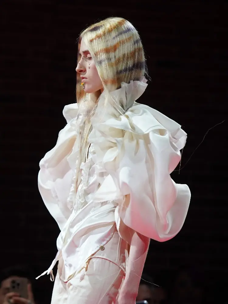Modelo en pasarela con cabello largo de varios tonos rubios y claros distribuidos en bandas visibles, mostrando un efecto de coloración multidimensional.