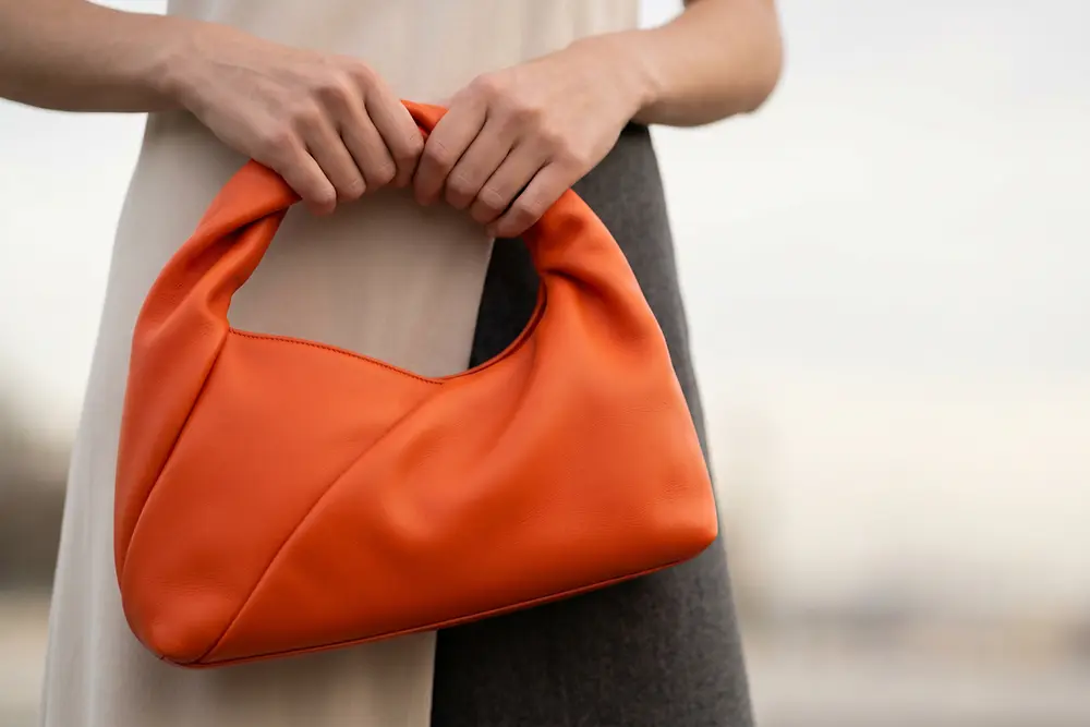 Bolso de cuero naranja sostenido por una persona, ejemplo de aplicación de las soluciones de recubrimientos especiales de Stahl para el sector de la moda y el lujo.