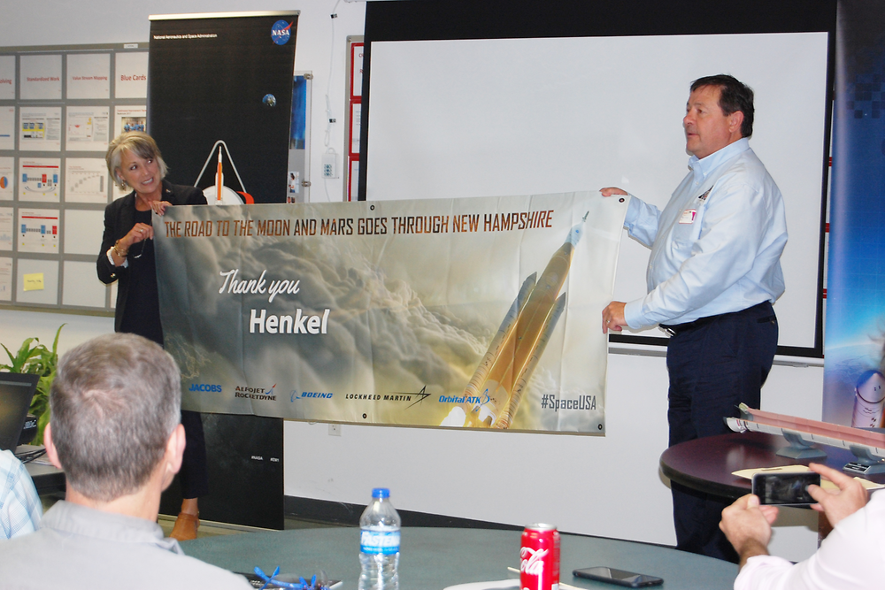 Marcia Lindstrom of NASA and Mark Olsen of OrbitalATK present Henkel with a commemorative banner for their partnership in creating materials used in NASA’s Space Launch System (SLS) project.