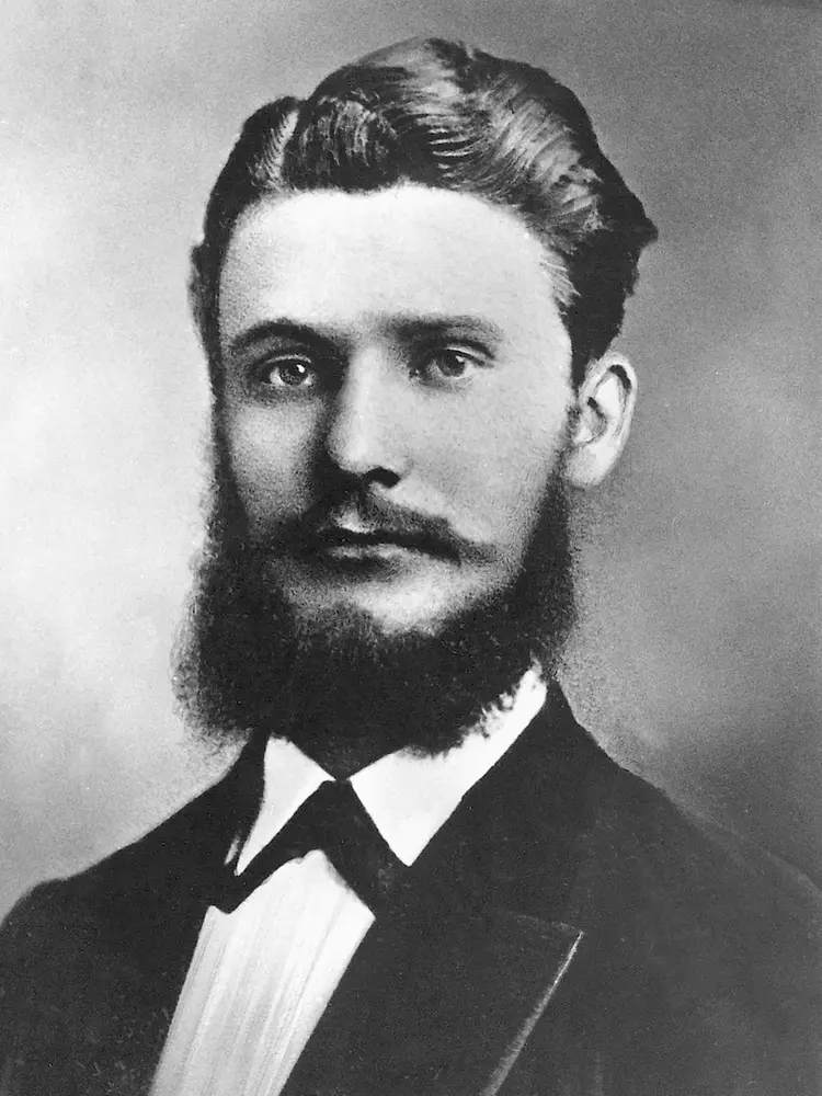 Retrato histórico en blanco y negro de Fritz Henkel con atuendo formal, barba completa y cabello peinado.
