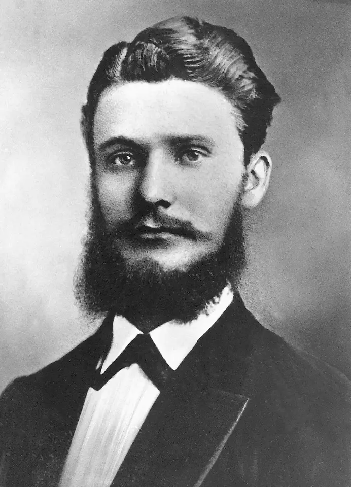 Retrato histórico en blanco y negro de Fritz Henkel con atuendo formal, barba completa y cabello peinado.